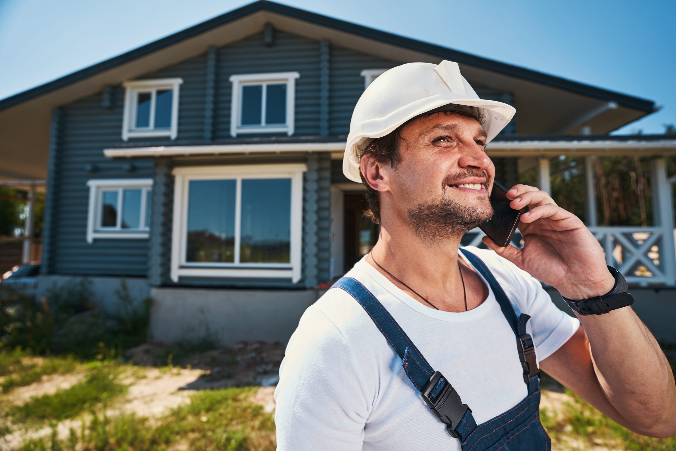 Happy worker chatting on mobile phone near house